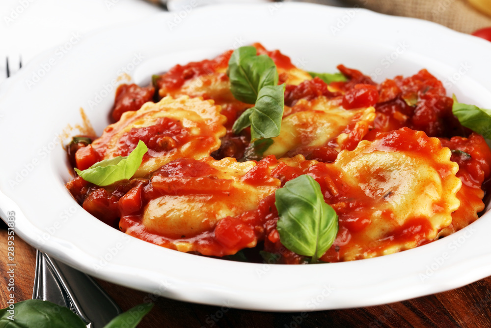 Ravioli with tomato sauce garnished with parmesan cheese and basil on rustic table