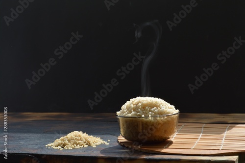 brown rice milled rice imperfectly cleaned unpolished rice in the bowl on a wooden table  black background photo