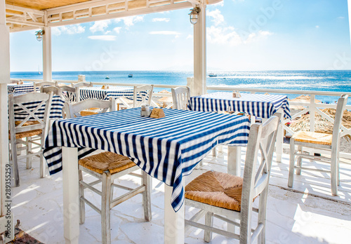 Beautiful view over traditional Greek tavern tables, blue sea and sky on the background. Food trip to Greece, Santorini concept. © FotoHelin