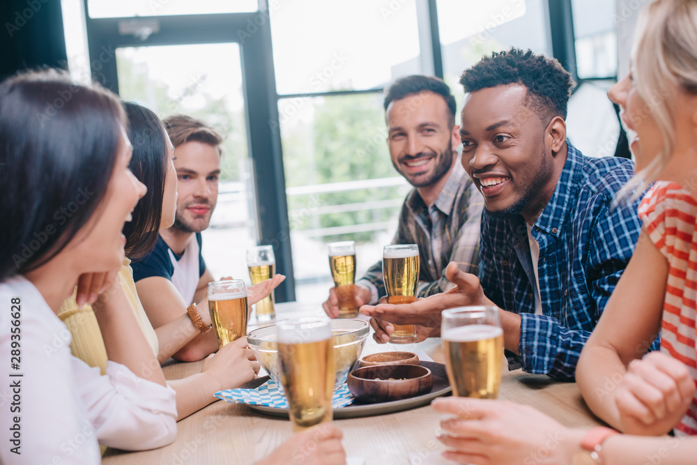 cheerful multicultural friends talking while sitting together in pub cheerful multicultural friends talking while sitting together in pub