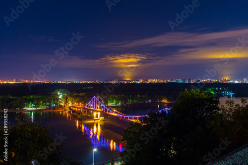 Night city landscape. A bridge across the river with bright colored lights. Landscape of the city of Kiev in the night. Night view of the capital of Ukraine