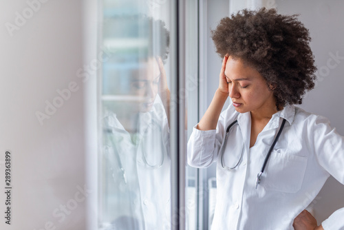 Φωτογραφία Sad female doctor leaning against the wall in hospital corridor