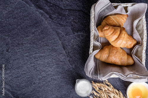 fresh croissants in a basket with a black slate background, top view.