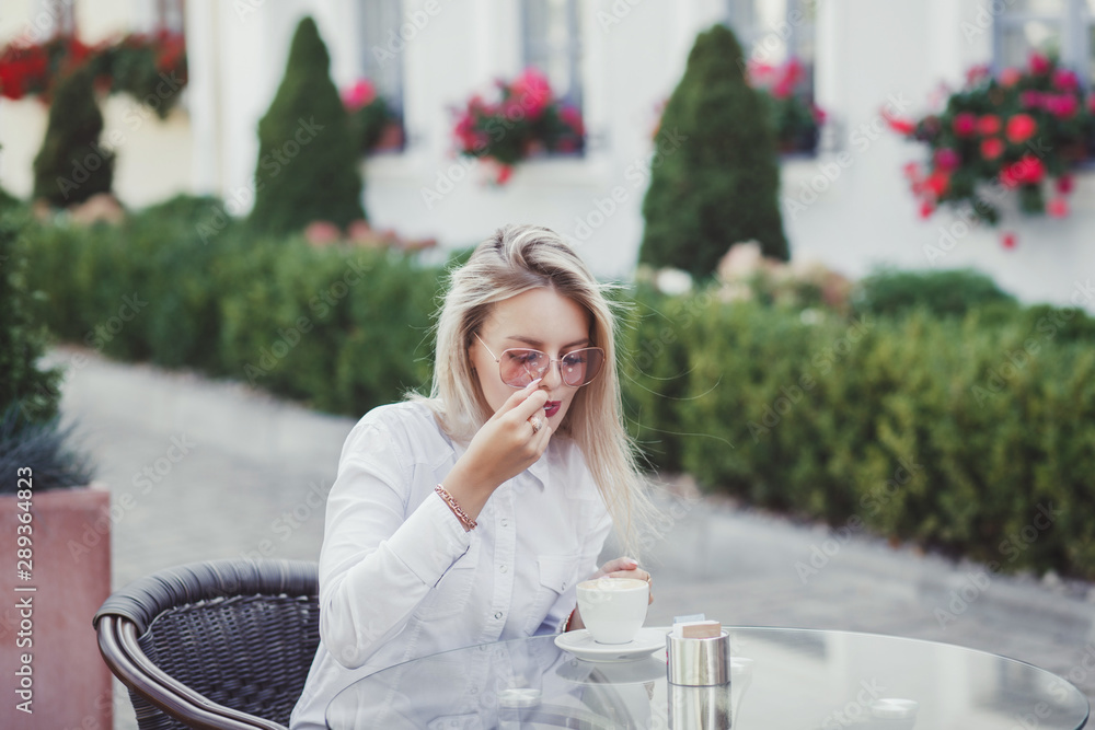 Stylish woman in the cafe sits at a table, drinks coffee 