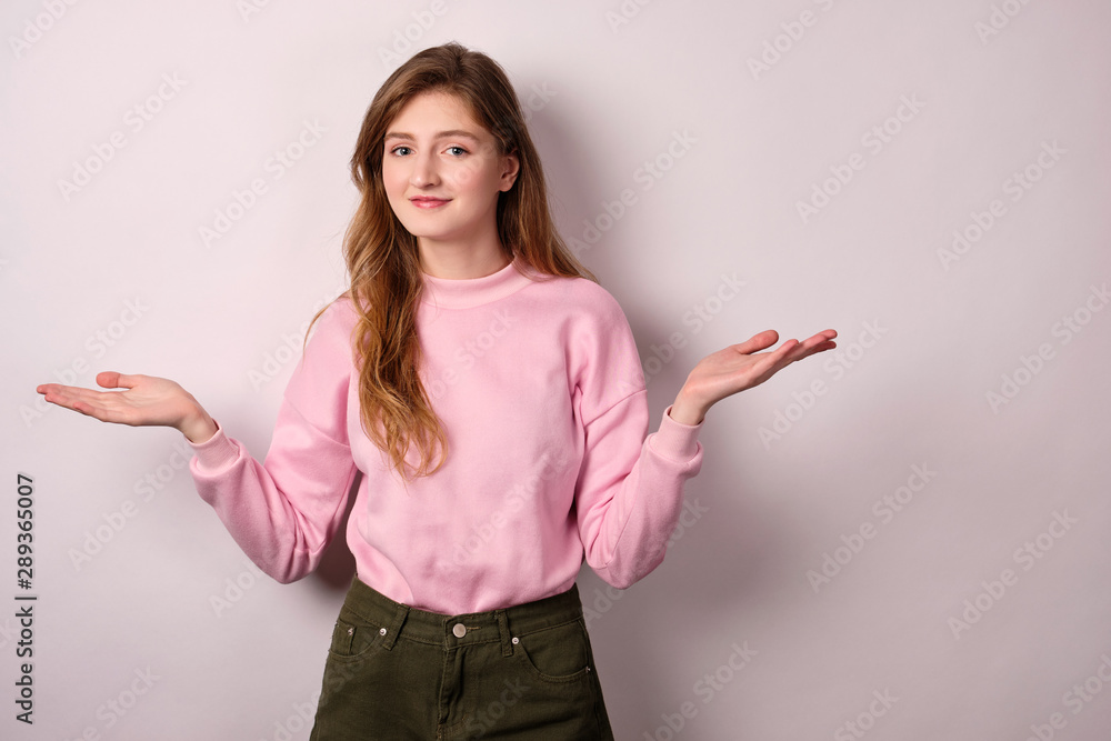 A girl in a pink sweater stands on a white background, looks at the camera, spreading her arms to the sides. A girl in a pink sweater stands on a white background, looks at the camera, spreading her arms to the sides.