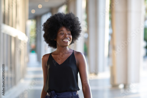 Smiling young black woman walking in the city enjoying the sunny day with her eyes closed