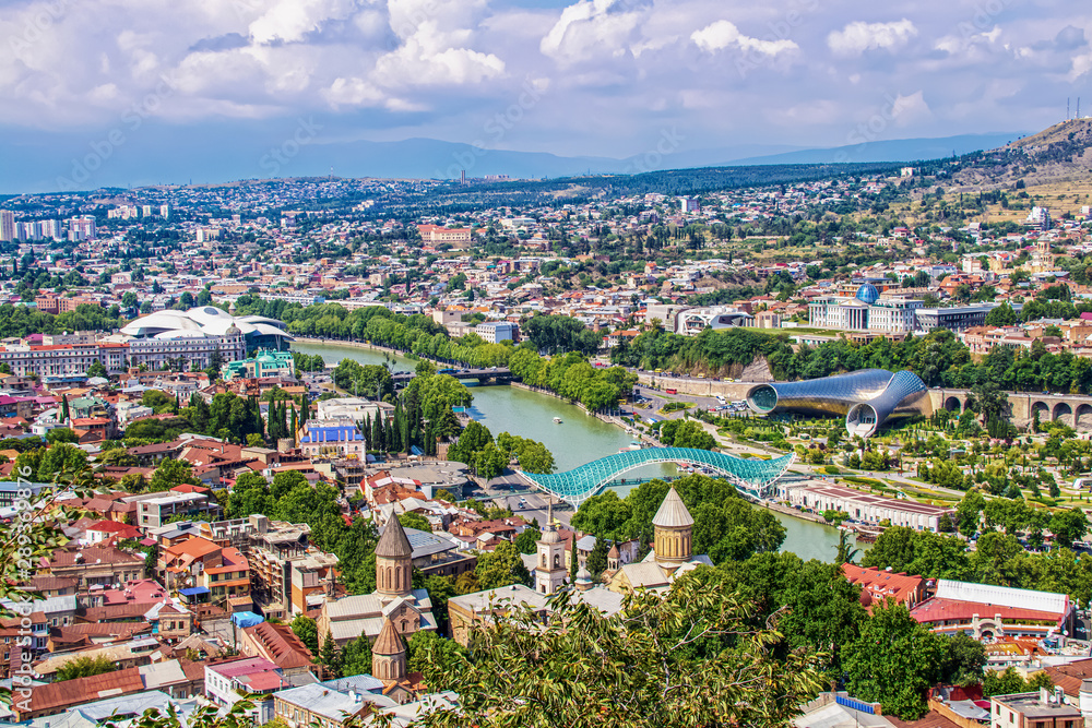 Aerial view of Tbilisi Georgia down the river Kura and the Bridge of Peace with both modern and ancient buildings on the skyline including the Capitol - Caucasus Mountains in distance