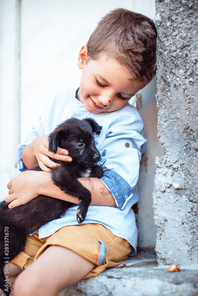 Obraz premium Cute boy holding his pet, little black puppy on the street. Kids and pets