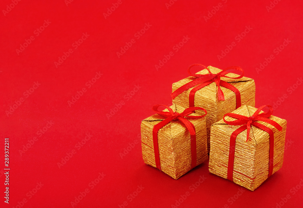 Stack of small golden gift box with red ribbon and bow on red background, with empty place for text on the left. Close up. Stack of small golden gift box with red ribbon and bow on red background, with empty place for text on the left. Close up.