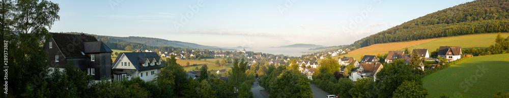 Wide panorama of a valley in Sauerland, Germany, with the spa village of Graftschaft and the pilgrimage Wilzenberg mountain at sunrise