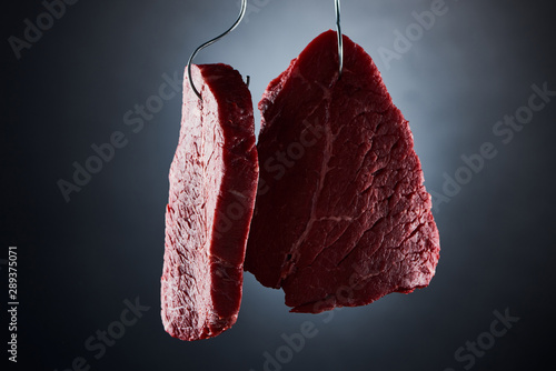 Quadro em tela raw beef sirloins on metal hooks on dark black background