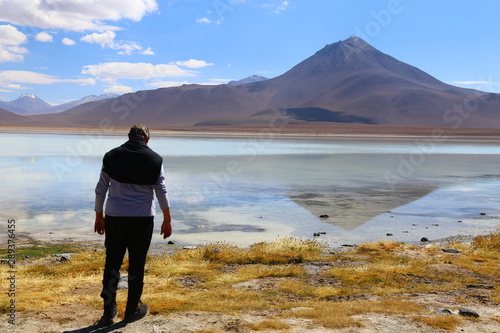 Man standing in front of the Laguna Blanca lake in Bolivia. White waters and reflections. In the background mountain and blue sky. 