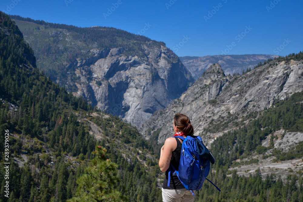 Young woman stands enjoying the view out over Yosemite National Park in the summer. Young woman stands enjoying the view out over Yosemite National Park in the summer.