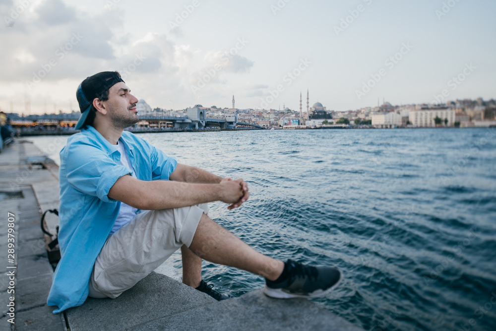 Portrait of a young man against the background of the sea, city, pier and ships.