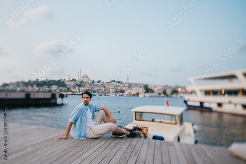 Portrait of a young man against the background of the sea, city, pier and ships. © Anna