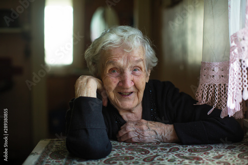 Portrait of a happy old woman sitting at a table in the house.