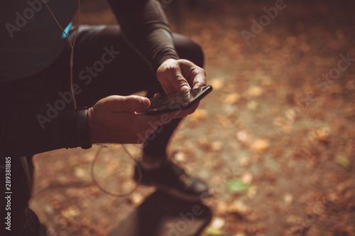 Fit man rest in the park after jogging he has earphone and mobile phone.