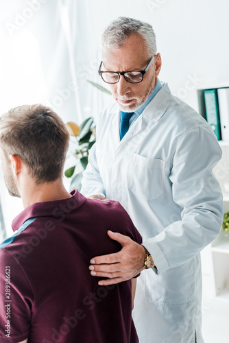 doctor in white coat touching back of patient in clinic