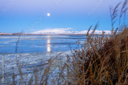 Evening autumn arctic landscape with river estuary covered with ice floes. Over the snowy hills a full moon. Autumn nature of Chukotka. Anadyr estuary, Chukotka, Far East Russia. October.