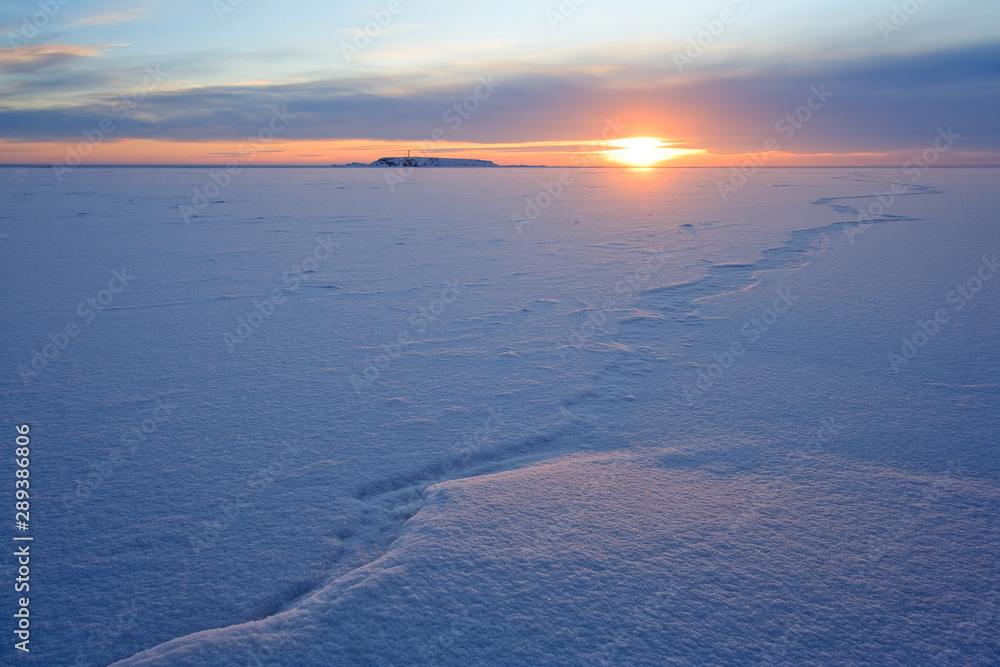 Winter dawn. Sunrise over a frozen bay. There are traces of a large crack in the ice. Far a small island. Arctic landscape. Cold polar climate. Anadyr estuary, Chukotka, Far East Russia. Extreme North