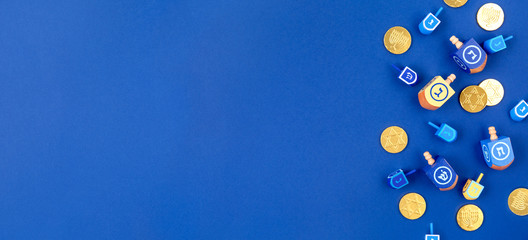 Dark blue background with multicolor dreidels and chocolate coins. Hanukkah and judaic holiday concept. Horizontal, banner format style