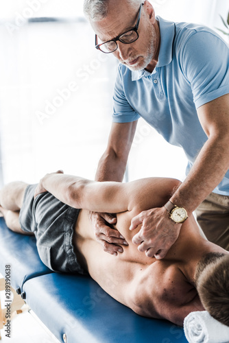 handsome chiropractor touching back of patient on massage table