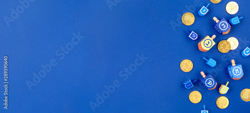 Dark blue background with multicolor dreidels and chocolate coins. Hanukkah and judaic holiday concept. Horizontal, banner format style photo