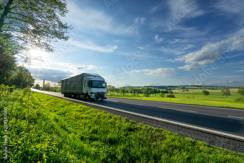 Obraz na płótnie White truck driving on the asphalt road in a green rural landscape w salonie