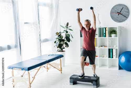 bearded mature man exercising with dumbbells in clinic photo