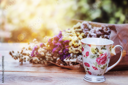 close up of a cup of tea and flowers on wooden table against sun light