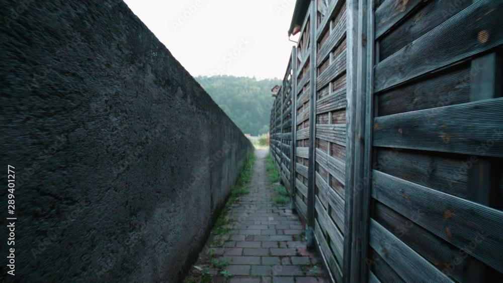 POV walking down a narrow path with walls at sides slow mov 4K. Person walk down a path between a stone and wooden wall. POV walking down a narrow path with walls at sides slow mov 4K. Person walk down a path between a stone and wooden wall.