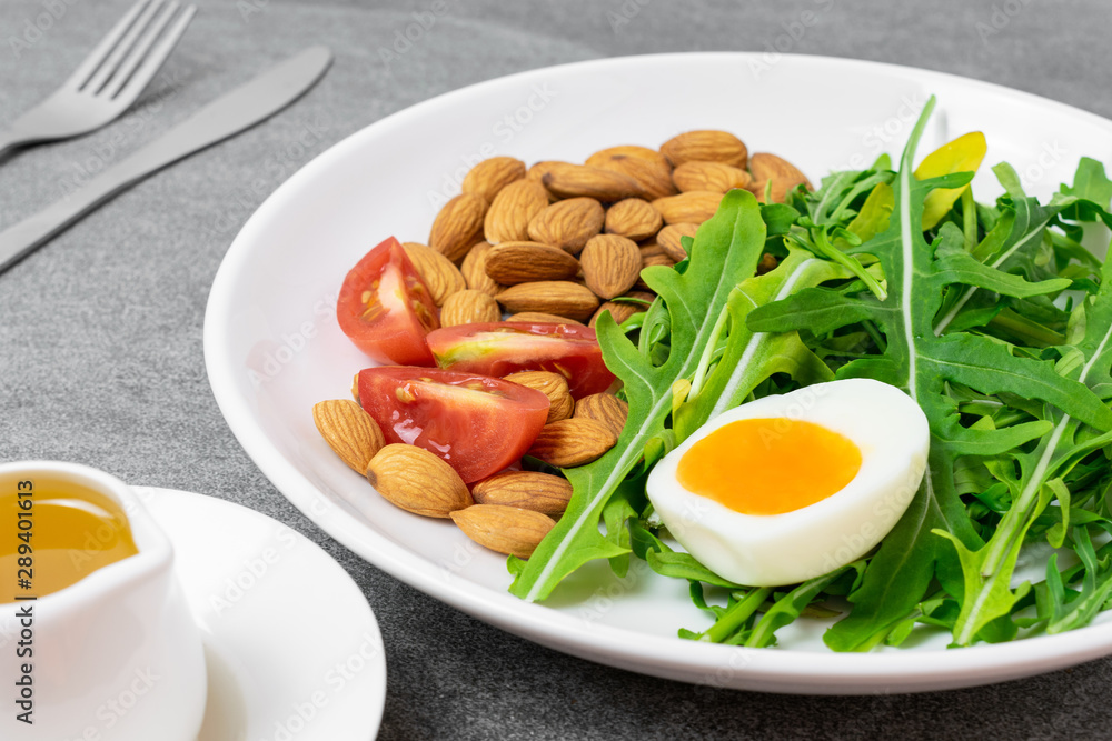 Arugula salad with almonds and tomato,boiled egg in white dish on tile table. Arugula salad with almonds and tomato,boiled egg in white dish on tile table.