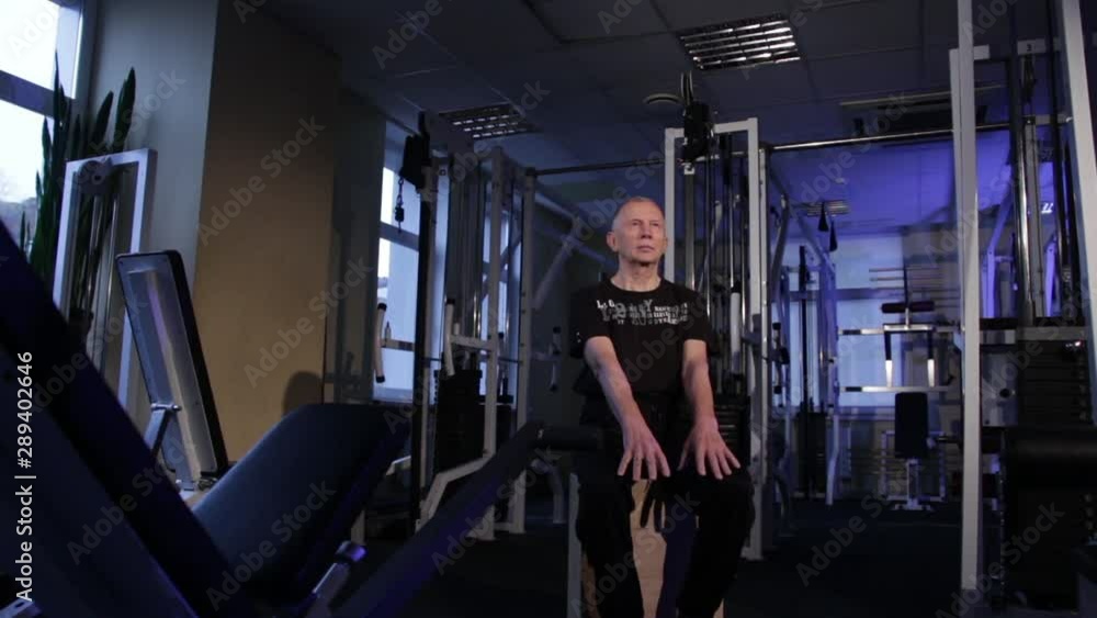 A man of the age performs joint gymnastics for the fingers in the gym.Clenching and unclenching your fist, arms out in front of you downstairs.Copy space. A man of the age performs joint gymnastics for the fingers in the gym.Clenching and unclenching your fist, arms out in front of you downstairs.Copy space.