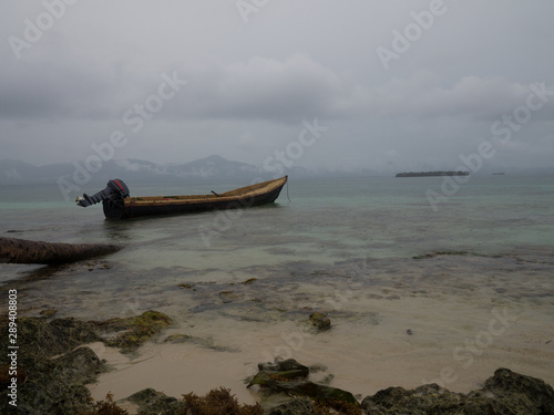Small boat anchored next to a palm log on a rainy day, mountain range on the background photo
