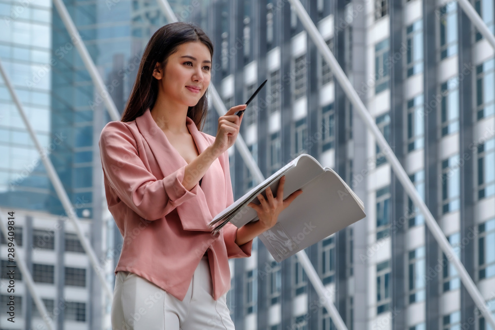 Fototapeta premium businesswoman is standing and working in front of office building in city