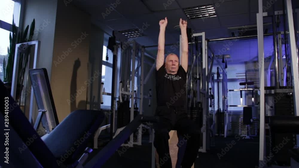 A man of the age performs joint gymnastics for the fingers in the gym.Clenching and unclenching your fist, hands up.Copy space. A man of the age performs joint gymnastics for the fingers in the gym.Clenching and unclenching your fist, hands up.Copy space.