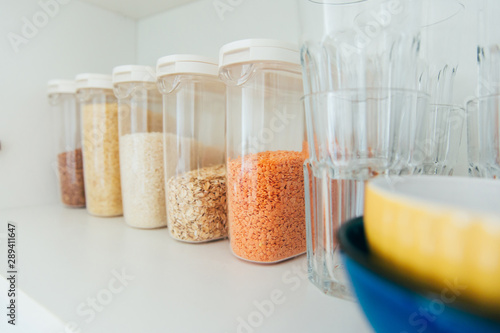 Various seeds in storage jars in pantry, white modern kitchen in background. Smart kitchen organization. Healthy cooking, clean eating concept.