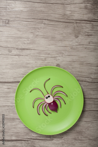 Funny vegetable spider made on green plate and wooden background