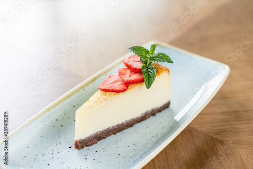 Piece of delicious cheesecake with strawberry and mint leaves on white plate.