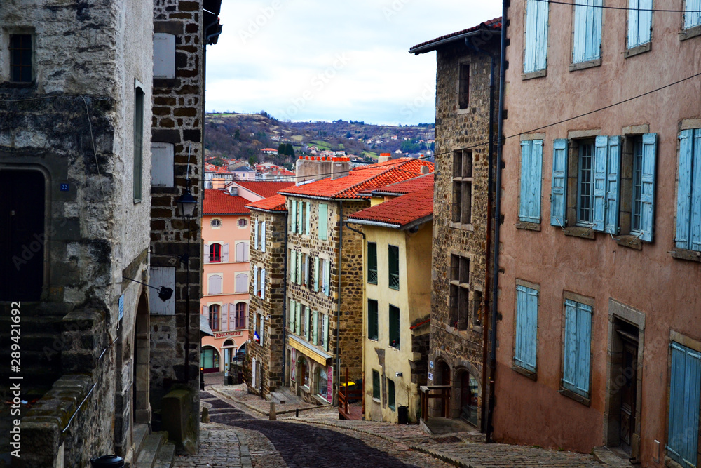 Le Puy-en-Velay, France - March 8th 2019 : View of a descending street, with a beautiful landscape on background. Le Puy-en-Velay is small enough to see nature from the city.
