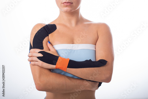 Female shoulder with kineziotape on a white background. Alternative medicine for sports injuries of joints and ligaments. Young sportswoman with medical record on a sore shoulder and wrist. photo