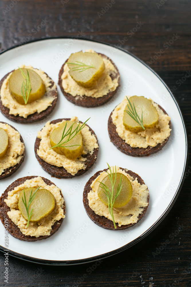 Pumpernickel rounds with hummus and pickled cucumber slices as snack. Pumpernickel rounds with hummus and pickled cucumber slices as snack.