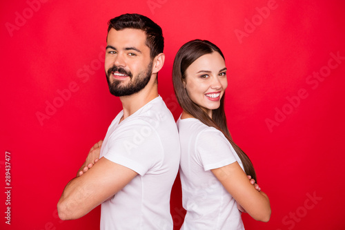 Photo of two casual trendy beautiful handsome pretty kind cheerful people standing back to back to each other wearing white t-shirts team while isolated with red background