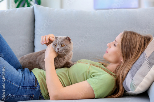 Beautiful woman with cute cat lying on sofa at home