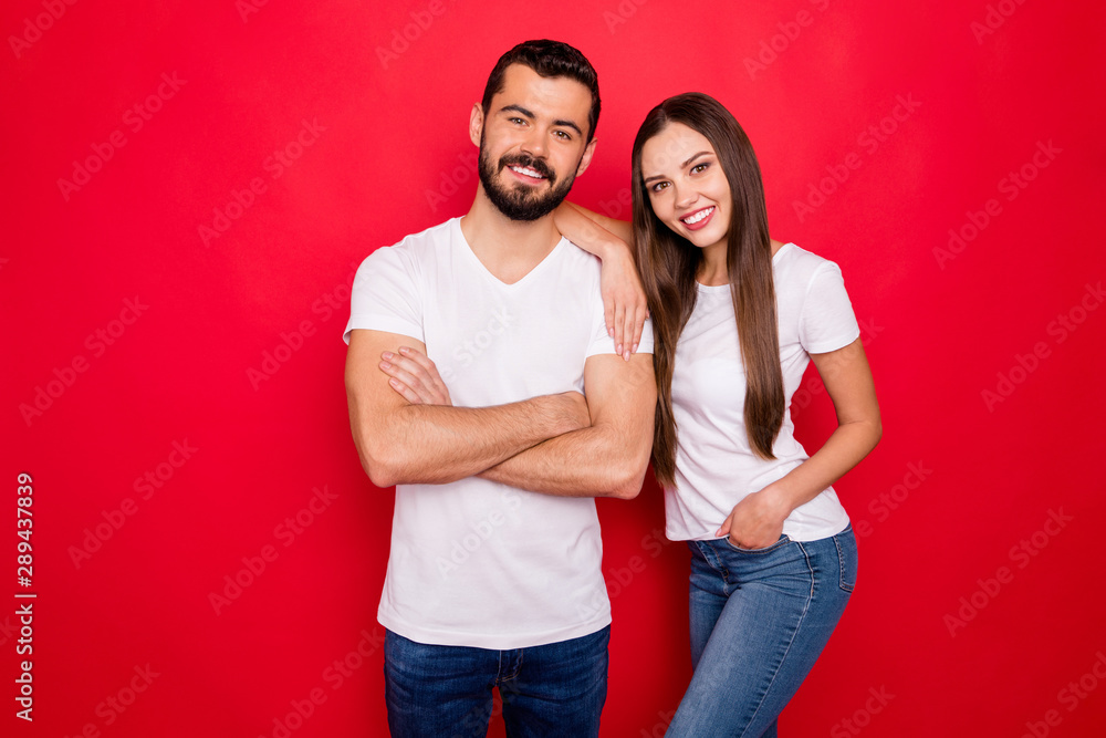 Photo of two casual charming cute pretty sweet people wearing jeans denim white t-shirts cheerfully looking while isolated over red background Photo of two casual charming cute pretty sweet people wearing jeans denim white t-shirts cheerfully looking while isolated over red background