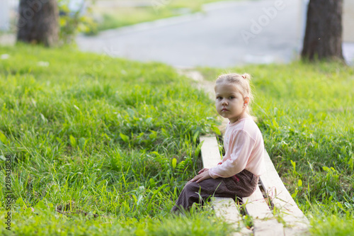 Little girl sitting on wooden bridge with legs dangling looking at camera