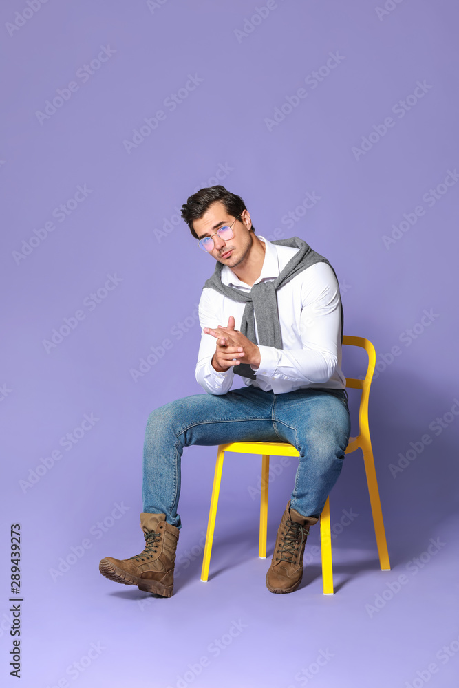Fashionable man sitting on chair against color background