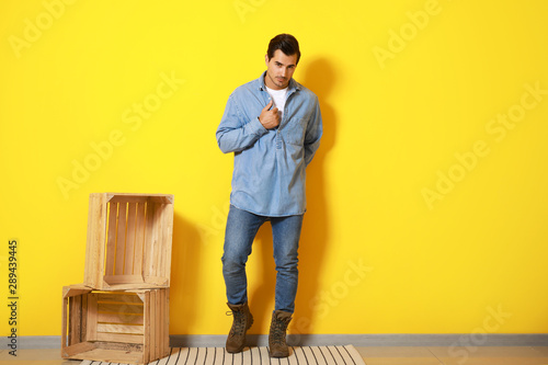 Stylish fashionable man and wooden boxes against color wall