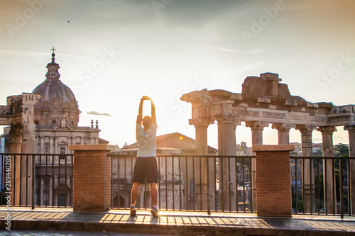 Young man exercising in front of the Roman Forum at sunrise. Historical imperial Foro Romano in Rome, Italy from panoramic point of view.