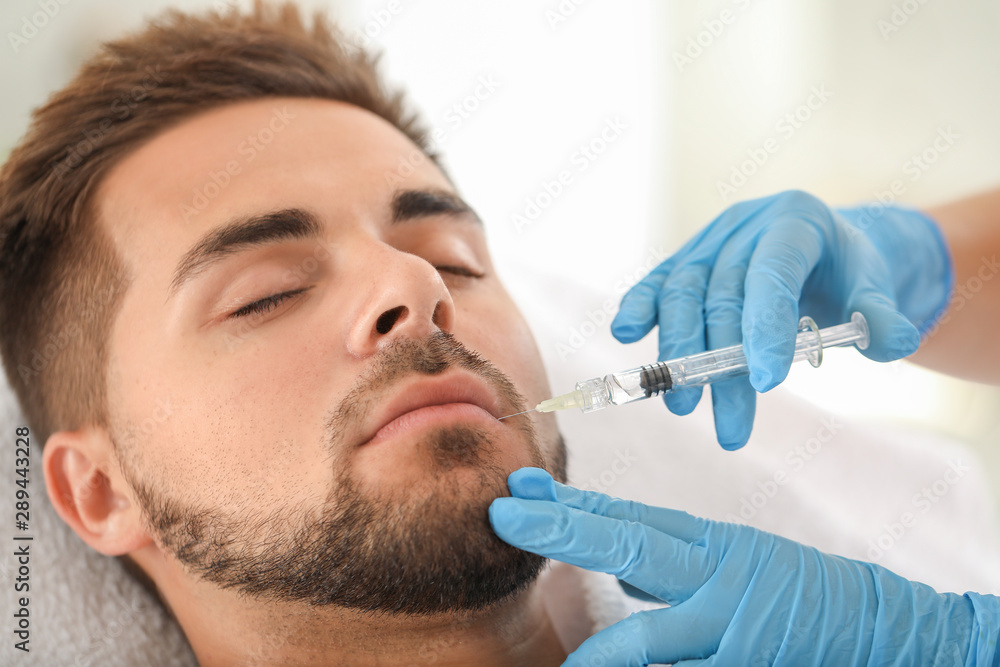 Handsome man receiving filler injection in beauty salon Handsome man receiving filler injection in beauty salon